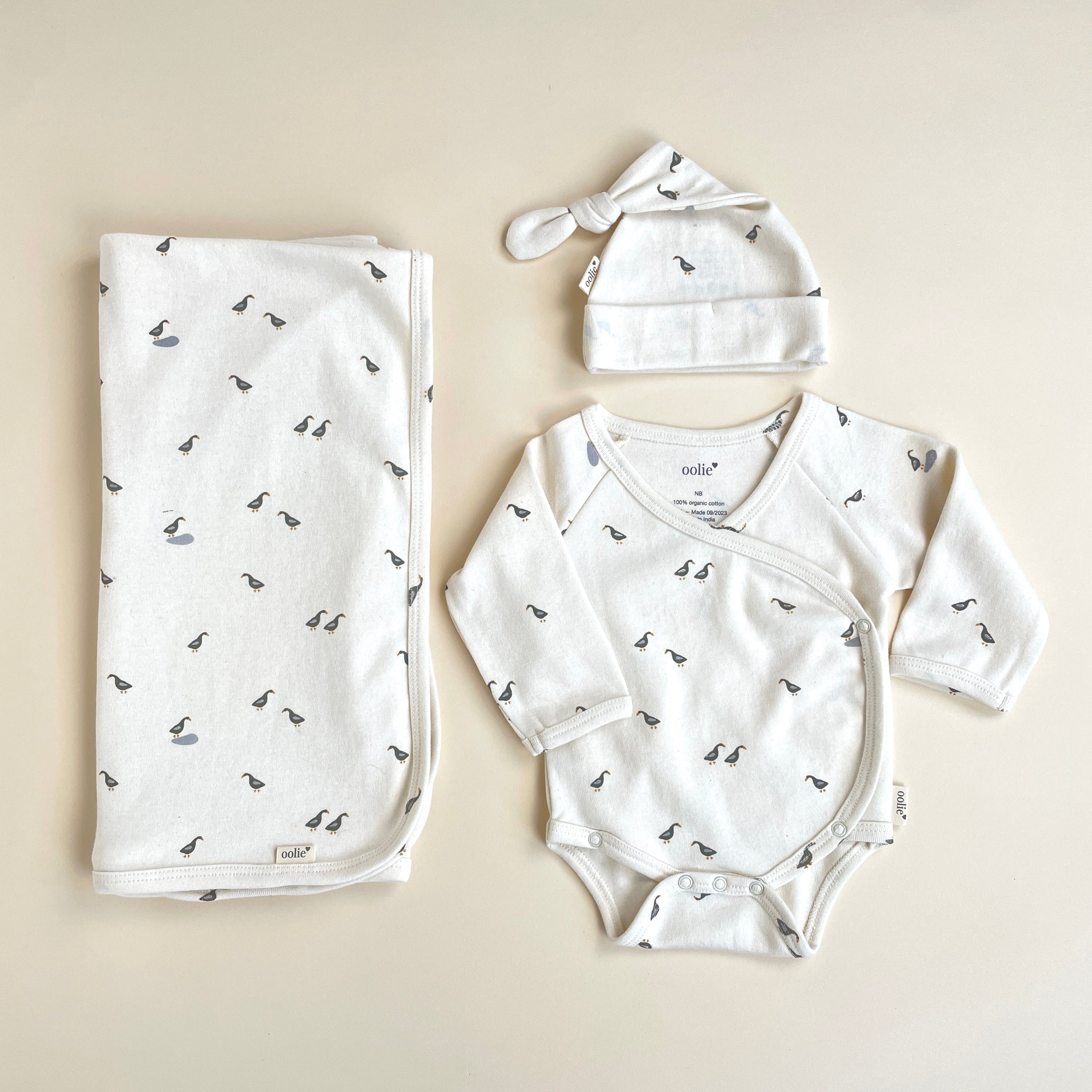 Baby clothing set with onesie, hat, and blanket on a beige background